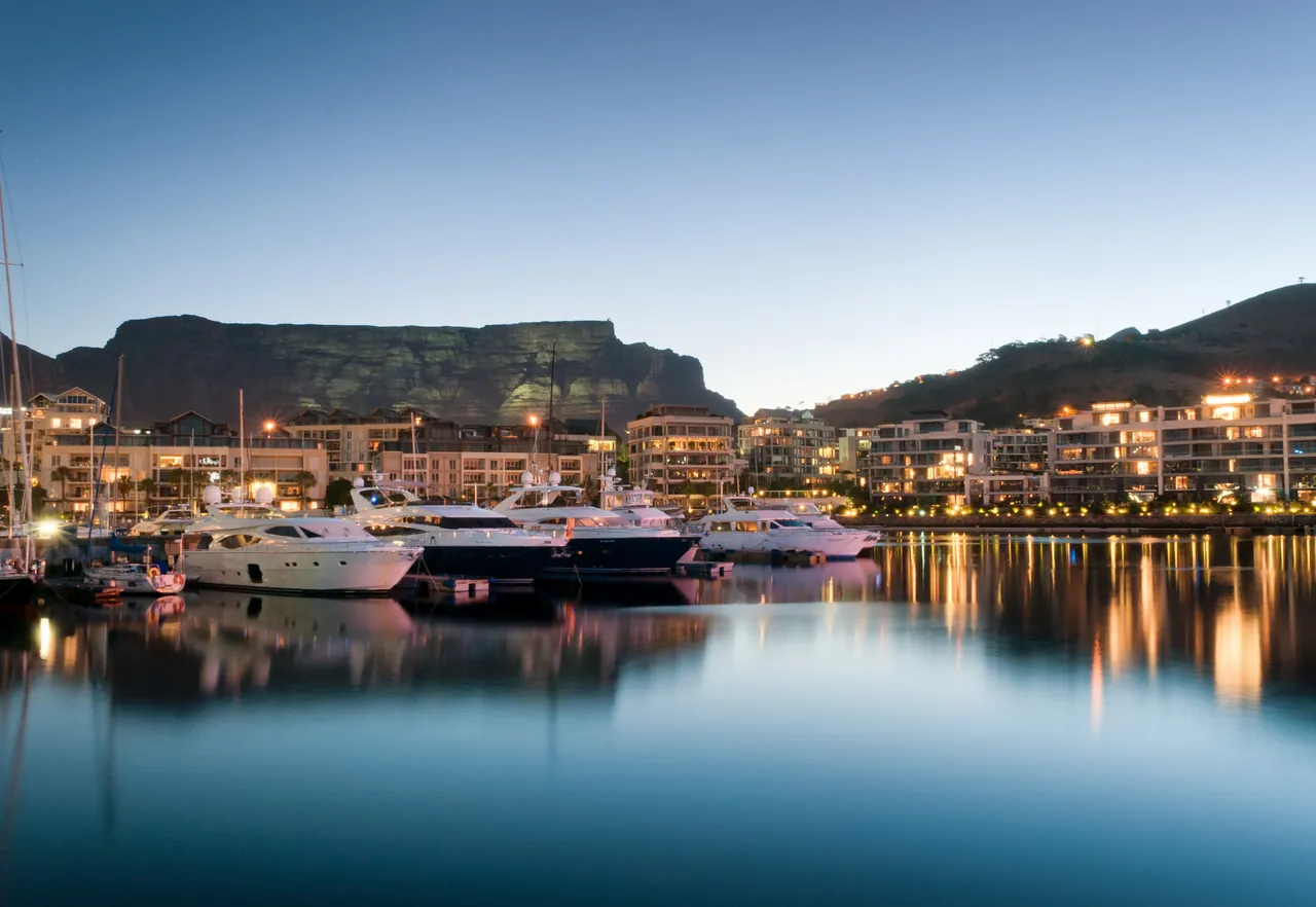 The V&A Waterfront marina lit up at dusk below Table Mountain, the area of The Portswood Hotel