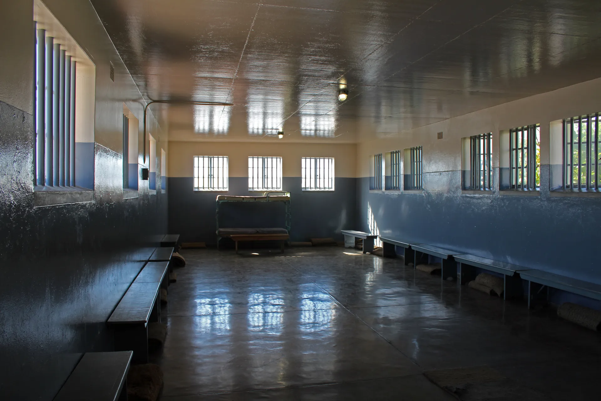 An empty communal hall with benches and barred windows in the prison
