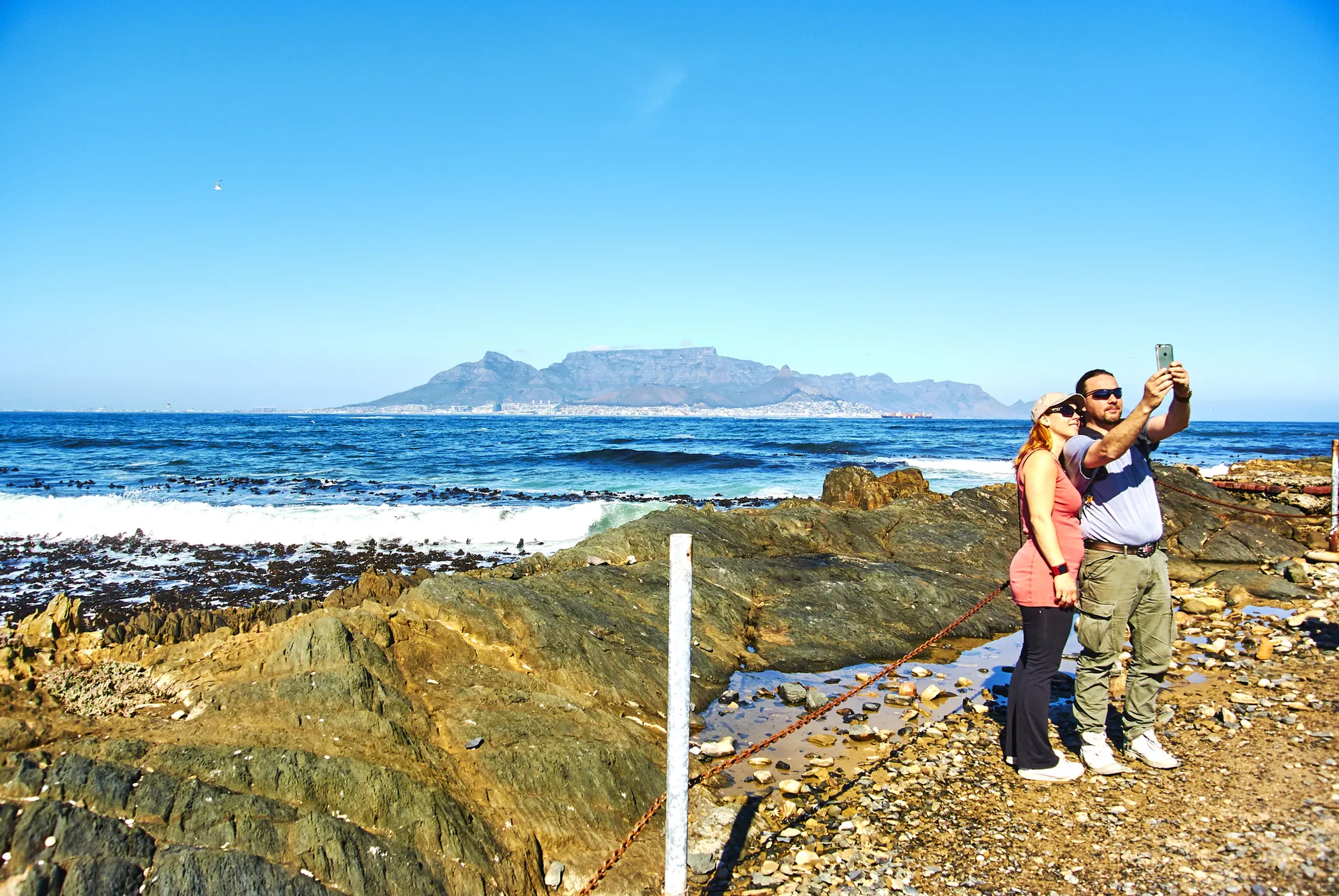 Visitors taking a photo on the rocky shore of Robben Island, with Table Mountain across the bay